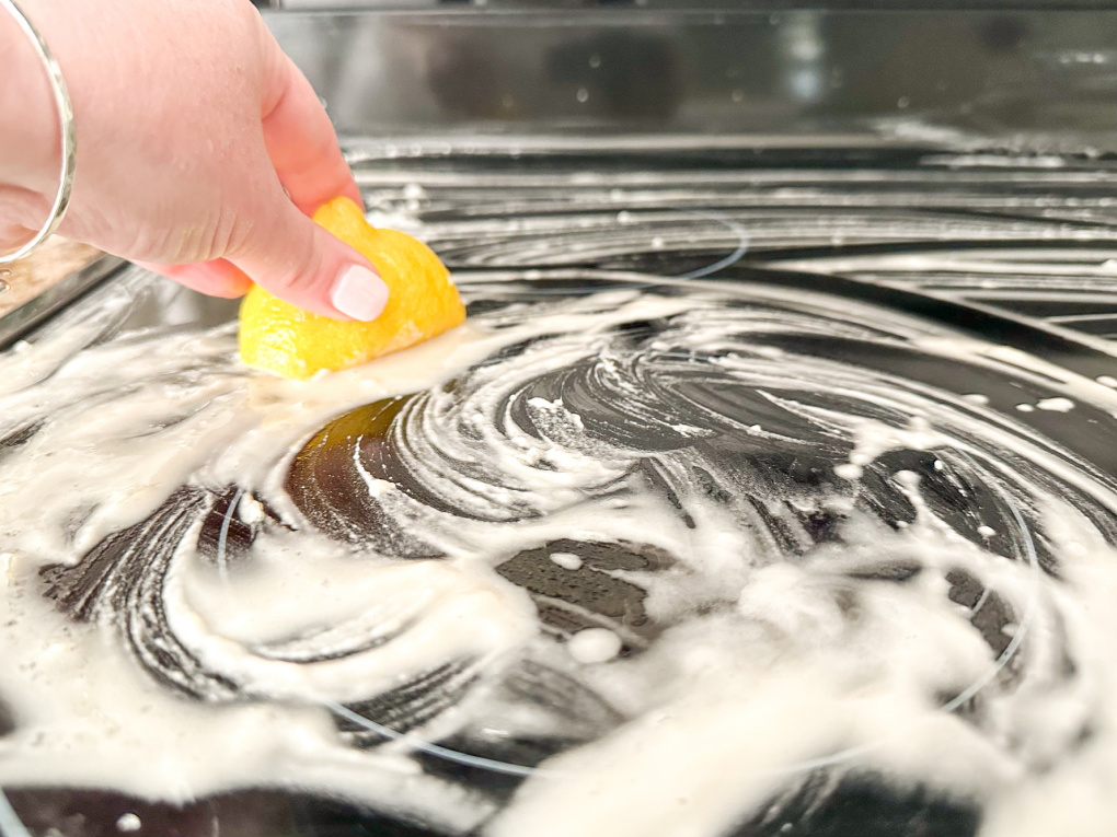 black glass stovetop being cleaned with baking soda , vinegar, and half of a lemon
