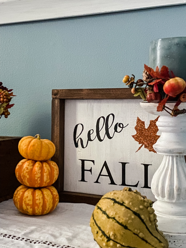 hello fall sign with mini orange pumpkins stacked on table.