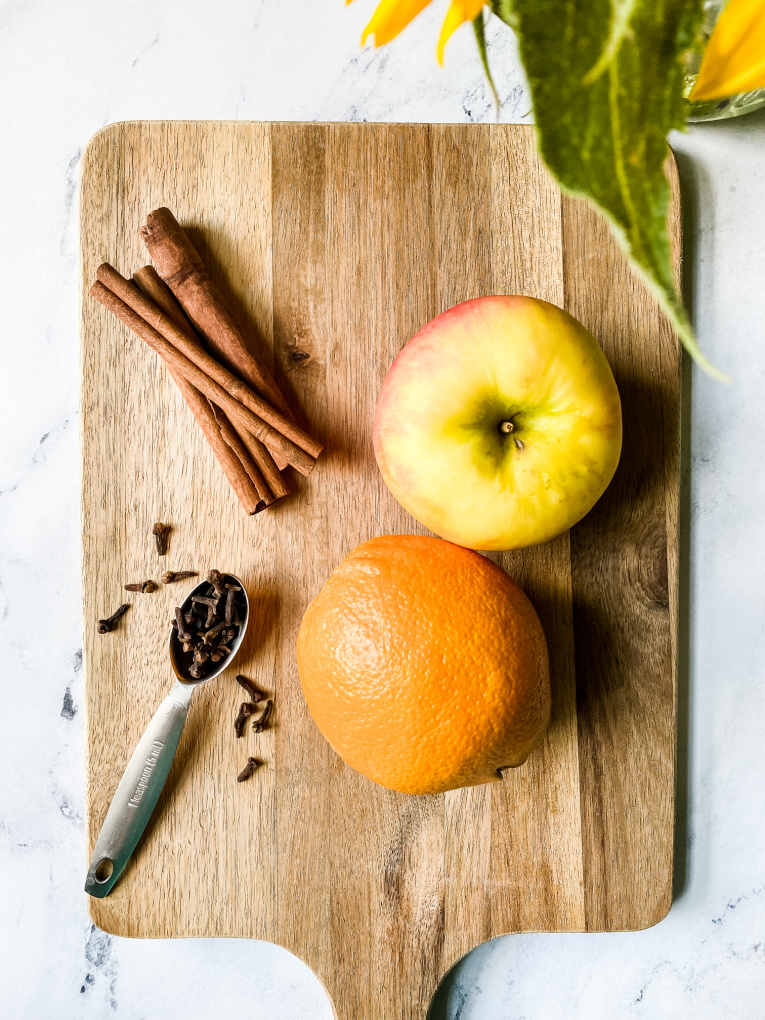 orange, apple, cinnamon sticks and cloves on a wood cutting board