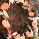 grapevine wreath with paper leaves, ribbon, and acorns on mantle with brick background