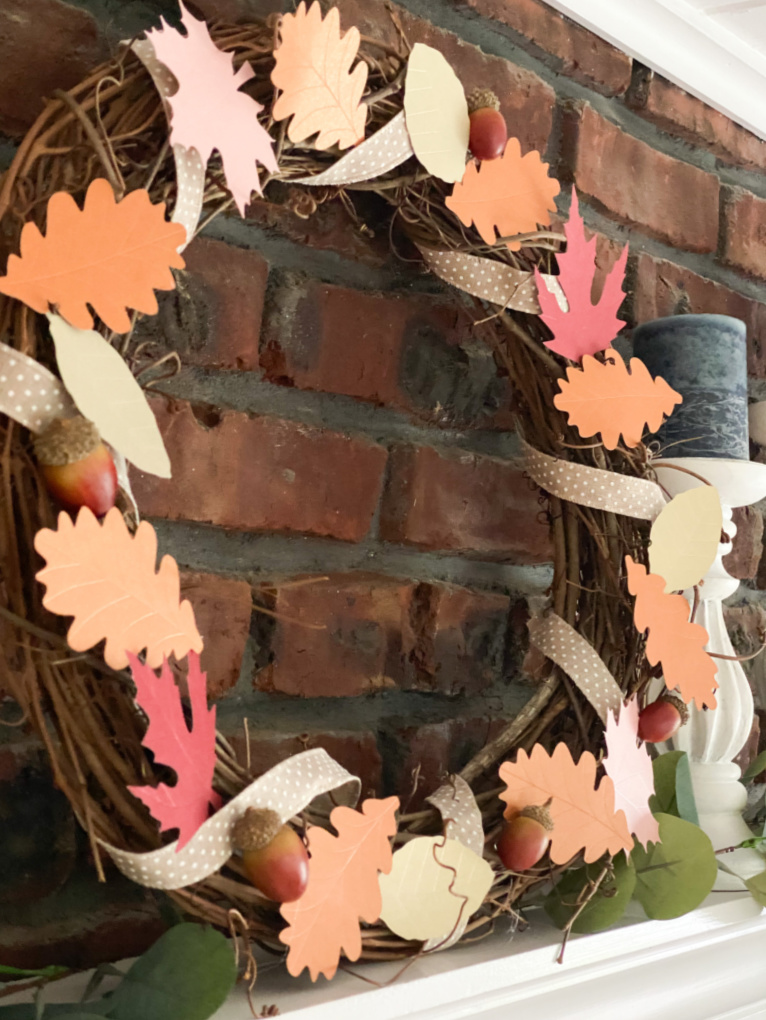 grapevine wreath with paper leaves, ribbon, and acorns on mantle with brick background