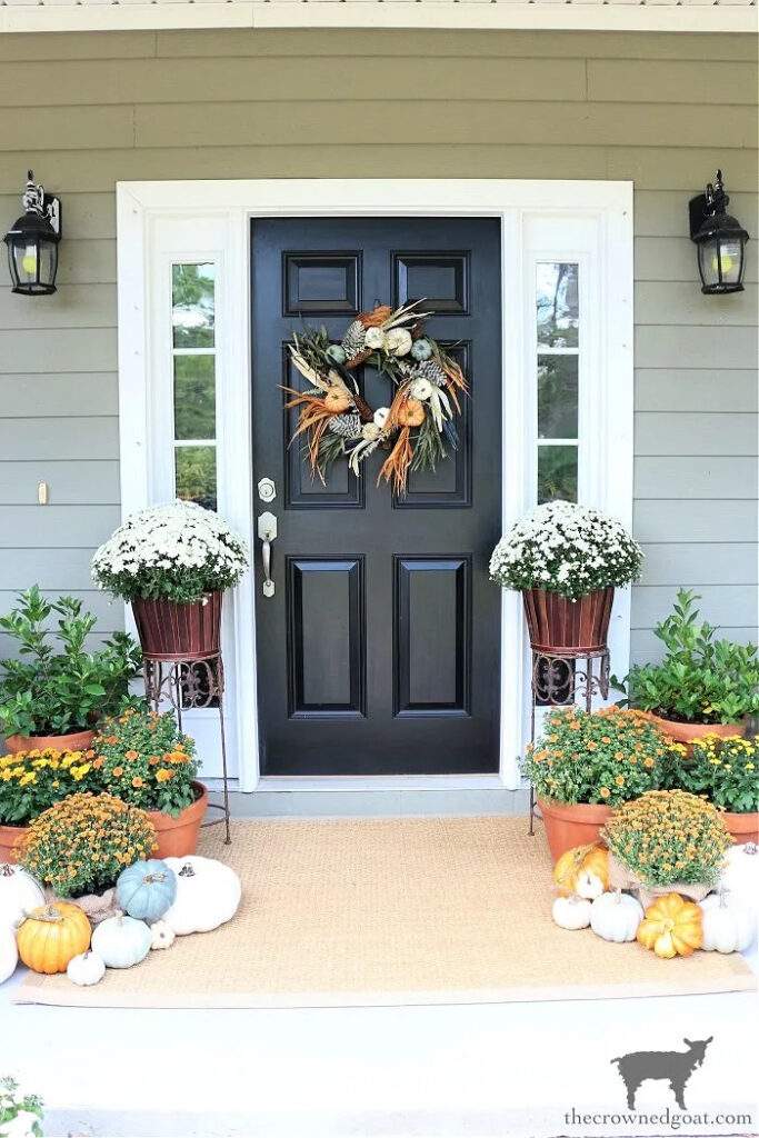 front door and porch decorated for fall with wreath and mums