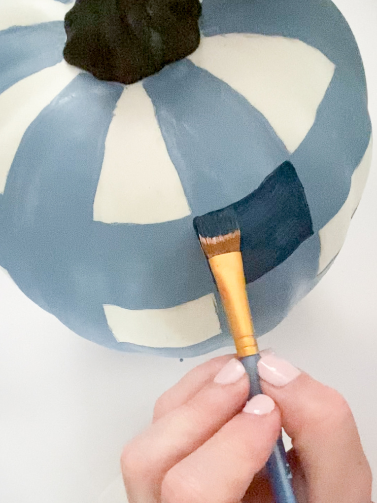 artificial white pumpkin in process of being painted in a gingham pattern