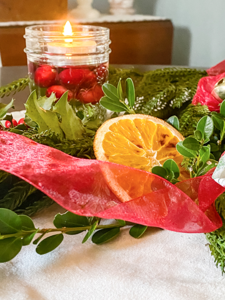 close up of Christmas garland on dining room table with ribbon and bells, greenery, and dried oranges