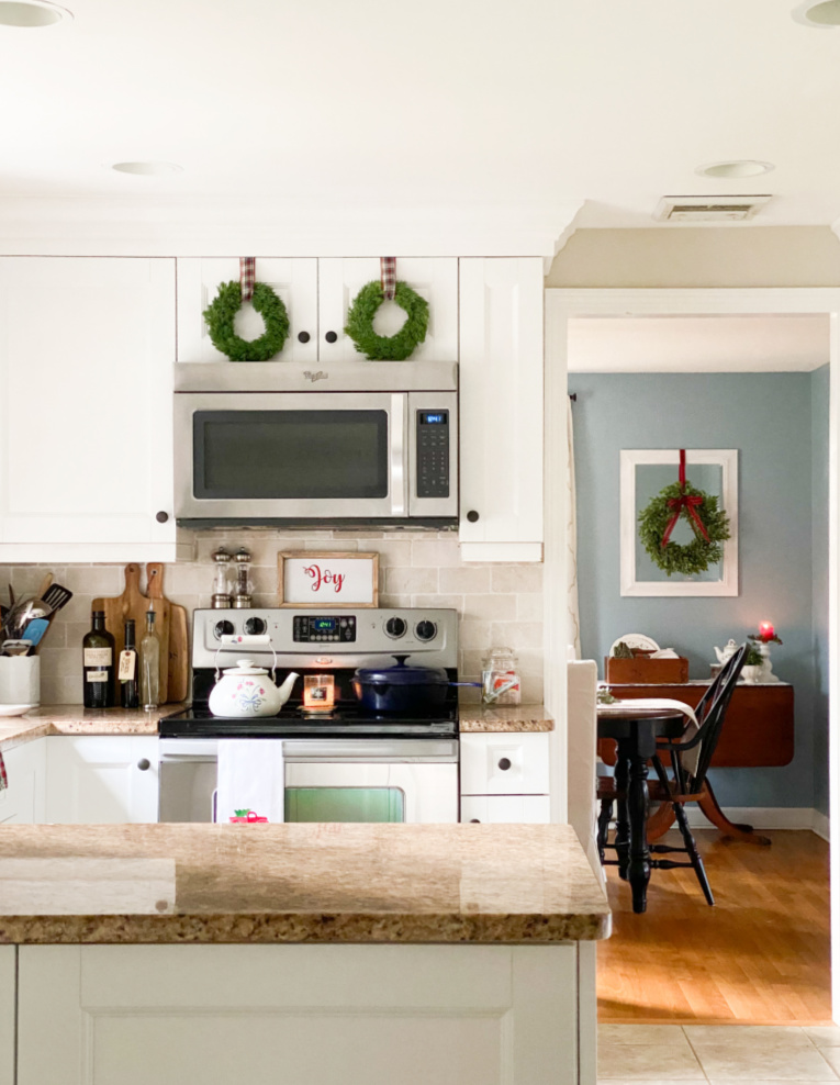 kitchen with white cabinets and Christmas wreaths on them.