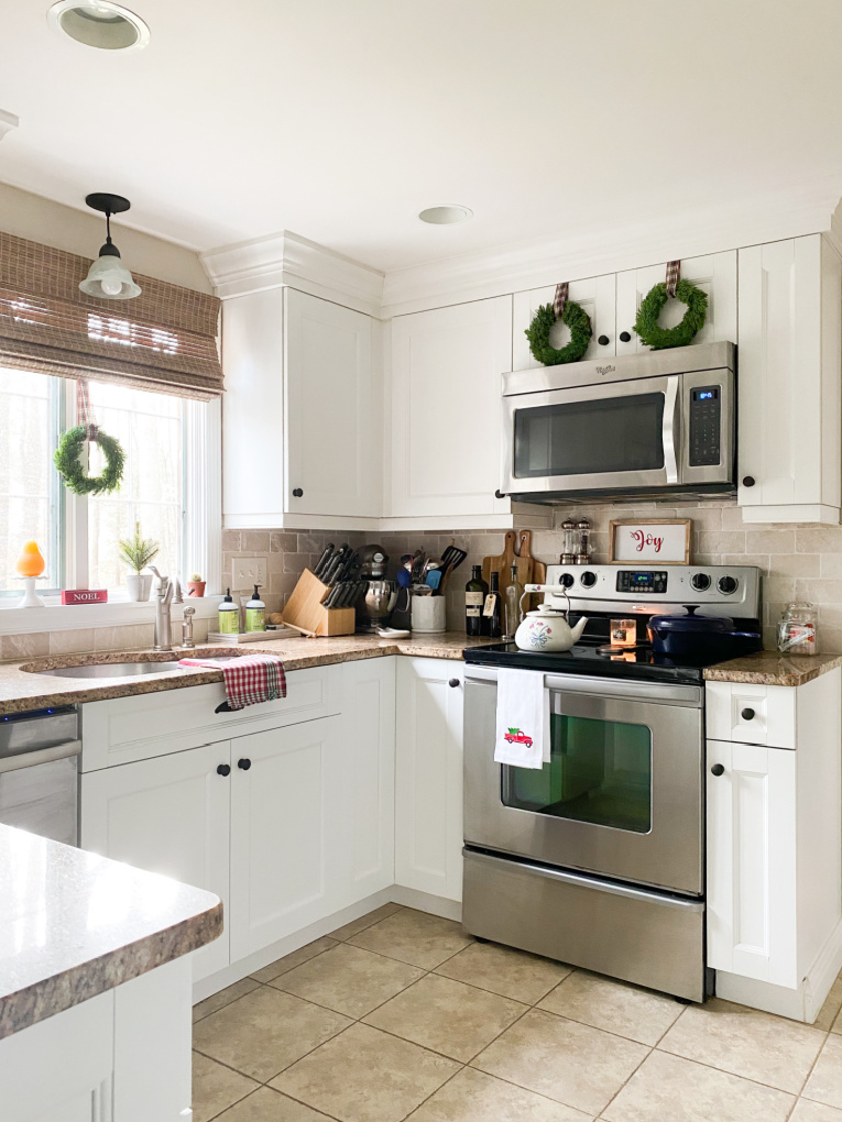 view of kitchen with white cabinets and wreaths hung on cabinets and window.