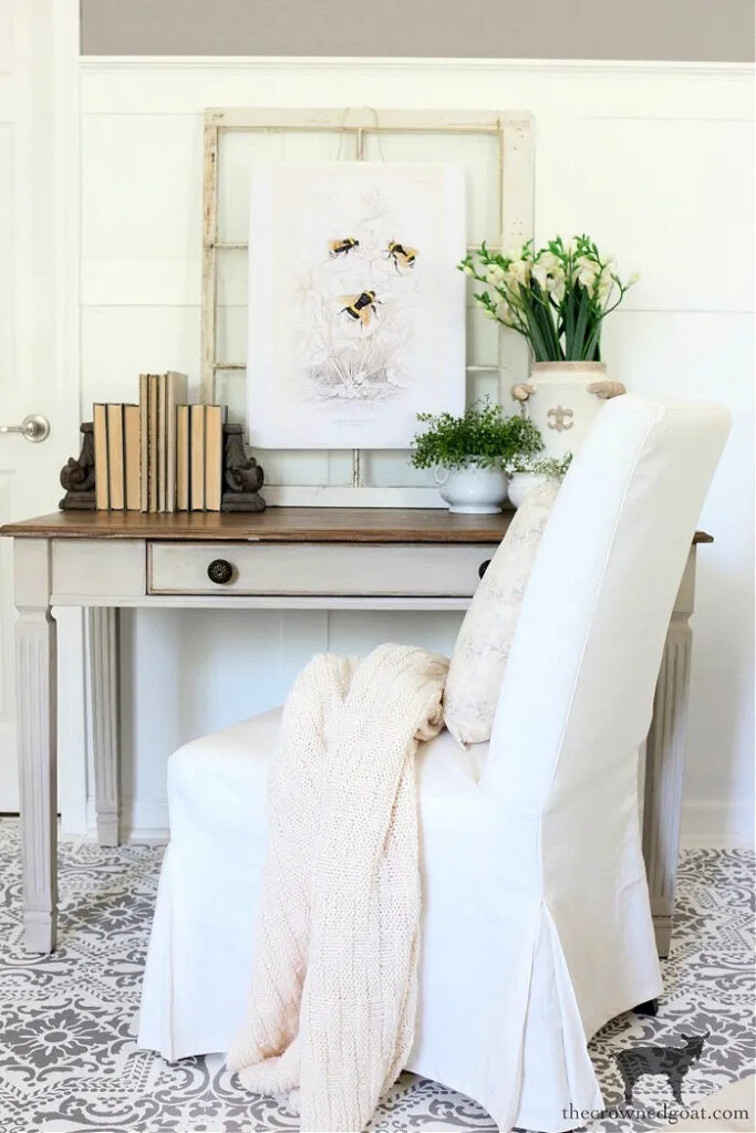 desk with books, bookends, flowers, and plants with parson's chair