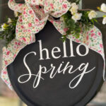 hello spring black painted pizza pan wreath with white lettering, floral bow, and greenery