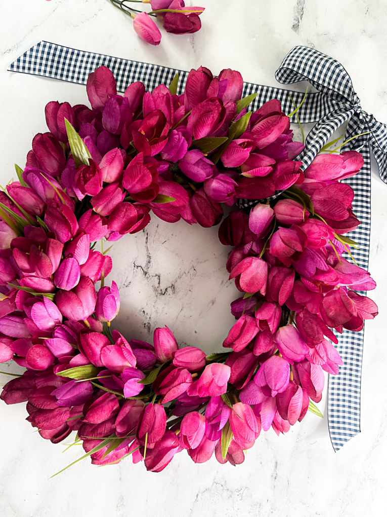 faux spring tulip wreath made with fuchsia faux tulips on marble counter with blue and white gingham ribbon