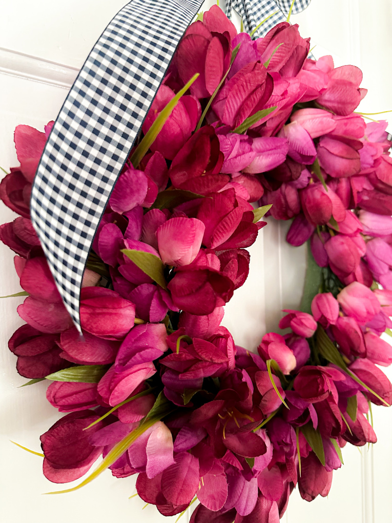 close up of faux spring tulip wreath made with fuchsia faux tulips hanging on a white door.