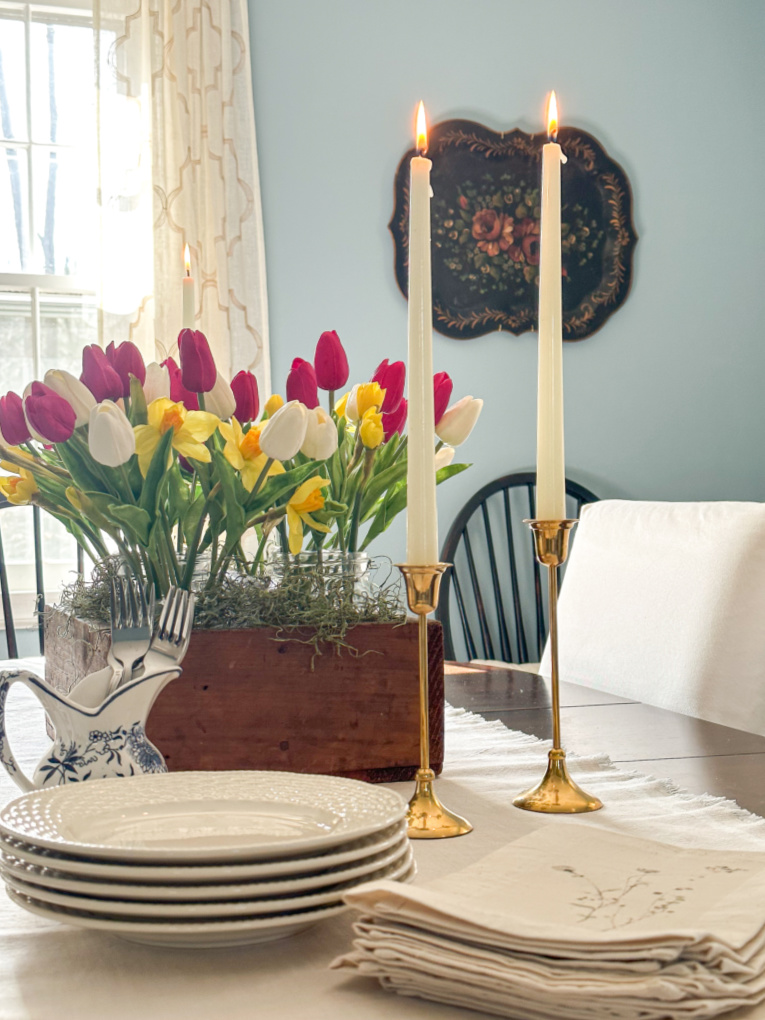 view of blue dining room with table set with candlesticks and tulip and daffodil arrangement in vintage tool box and dessert plates, forks, and napkins