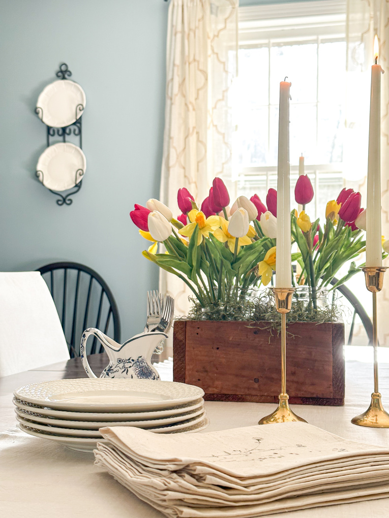 blue dining room with table set with candlesticks and tulip and daffodil arrangement in vintage tool box and dessert plates, forks, and napkins