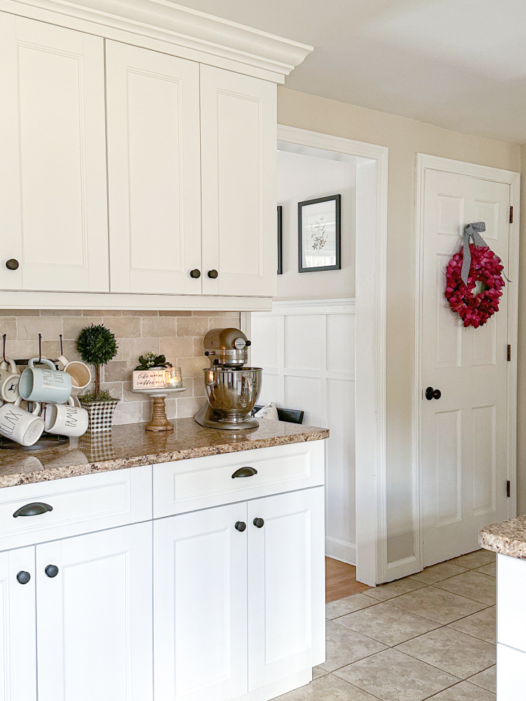 white kitchen cabinets and view into hallway with diy board and batten and fuchsia tulip wreath on the door