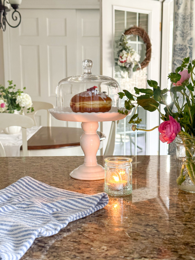 view of open back door from kitchen with raspberry paczki donuts with candle, pink ranunculus in mason jar and candle on kitchen counter