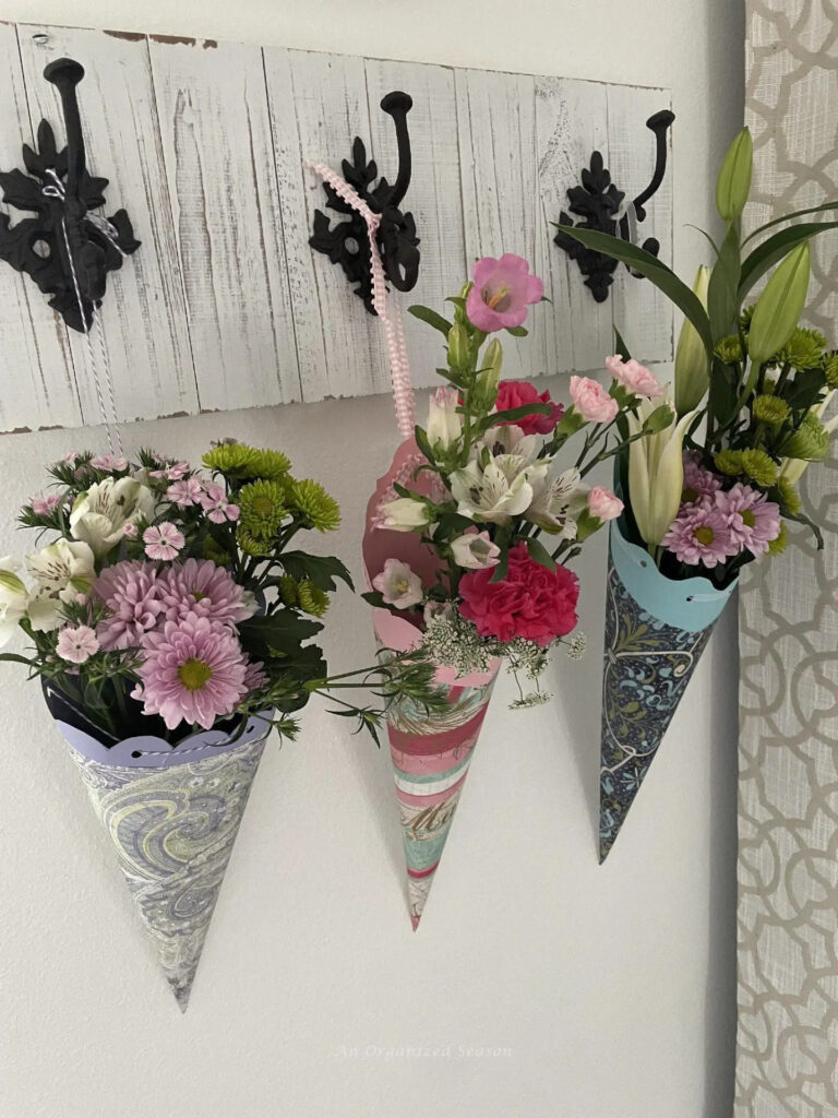 3 DIY May Day paper cones filled with fresh flowers hanging on hooks