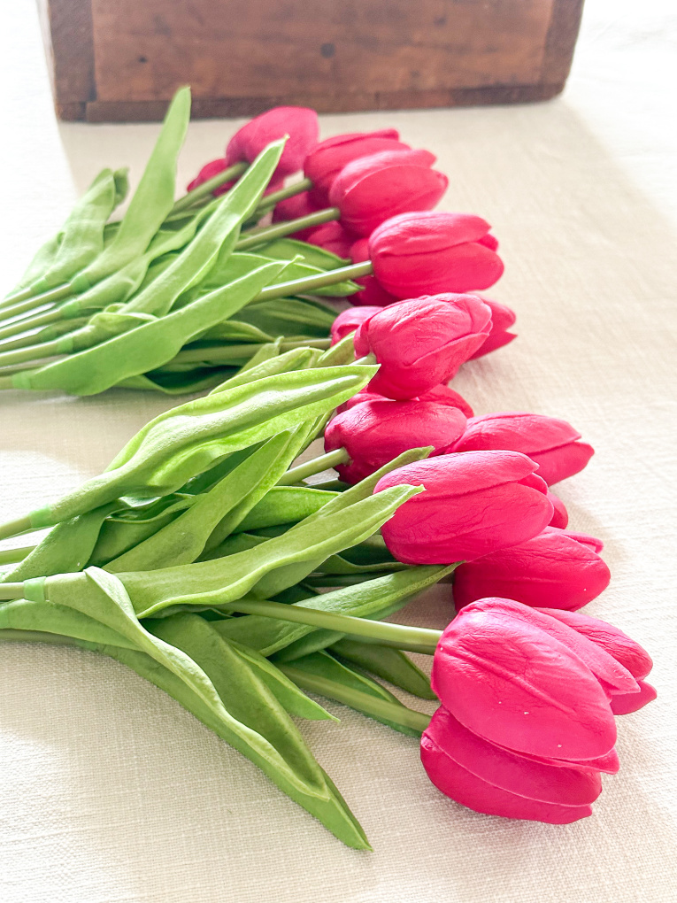 red artificial tulips in bunches on a cream colored table runner
