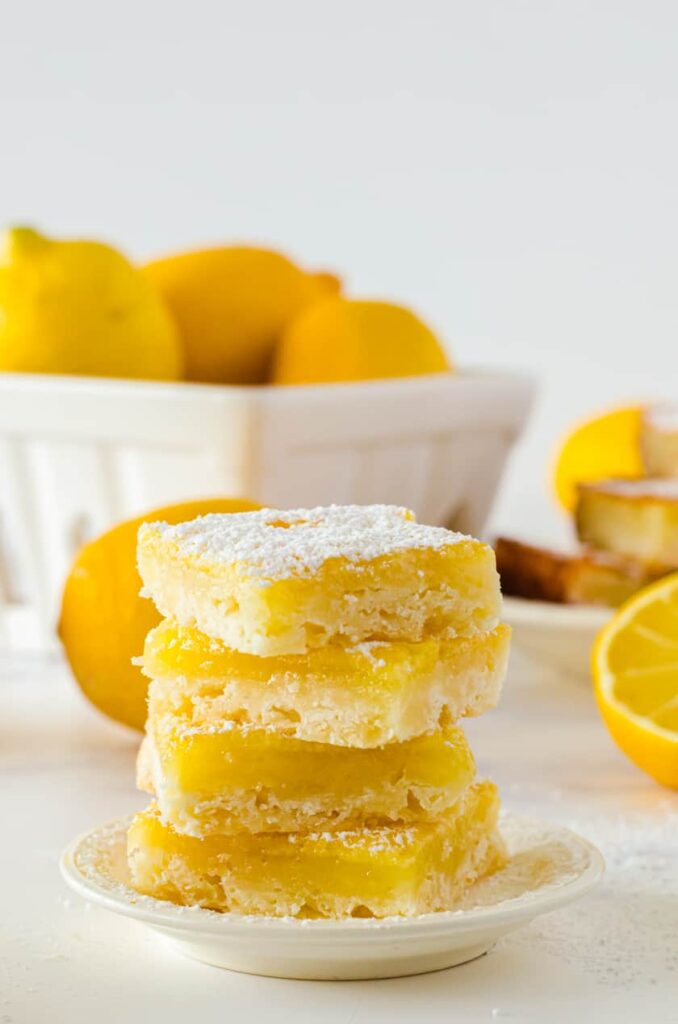 stack of 4 lemon bars on a plate with lemons in the background