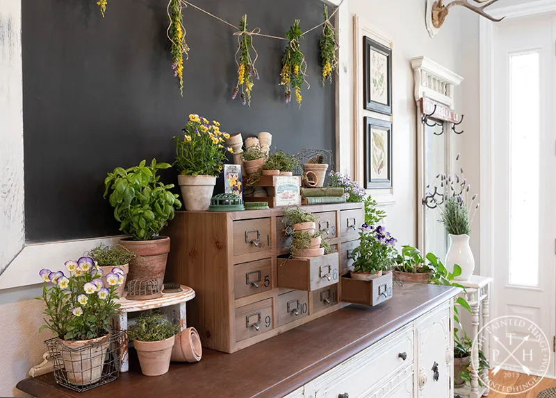 entryway table with chalkboard hung on wall, decorated with a variety of plants and herbs.