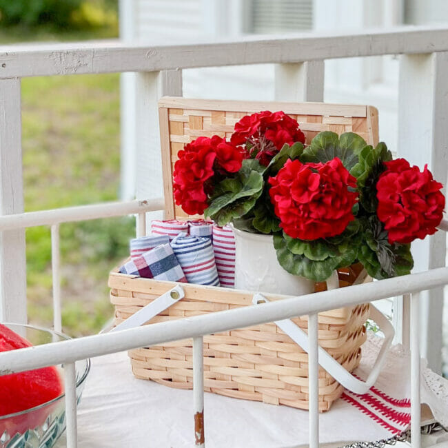 red geraniums in basket with rolled red, white, and blue towels.