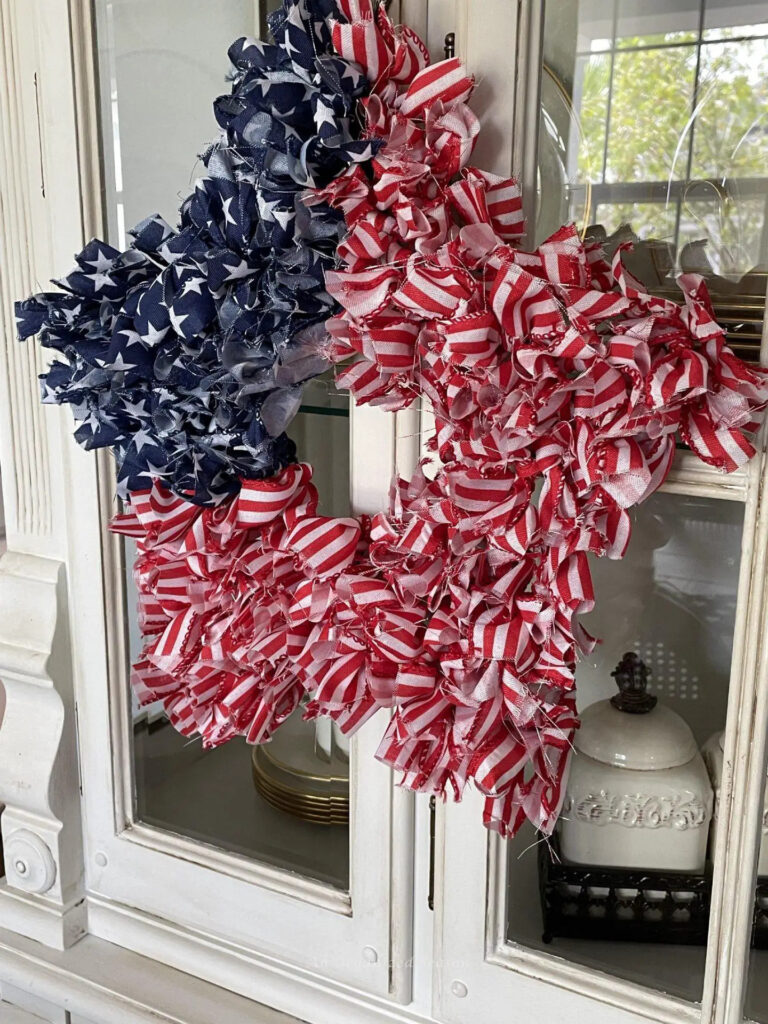 patriotic star shaped red, white, and blue ribbon wreath hanging on a white glass cabinet