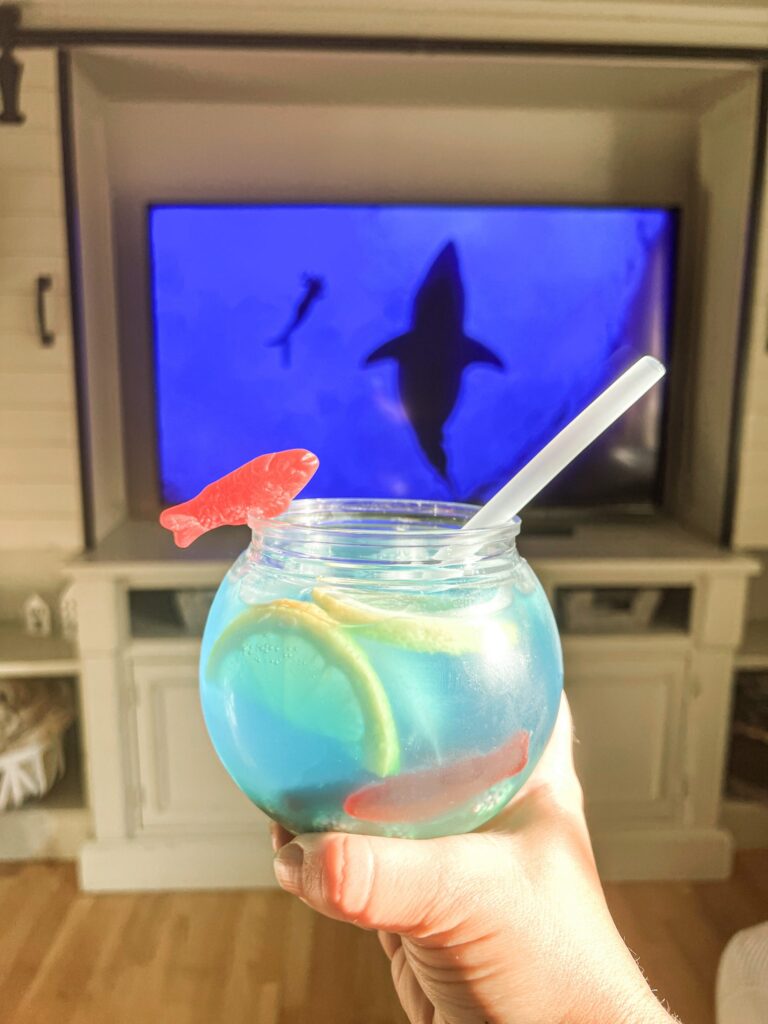 Shark week fish bowl drink in a glass in front of tv screen with a shark.