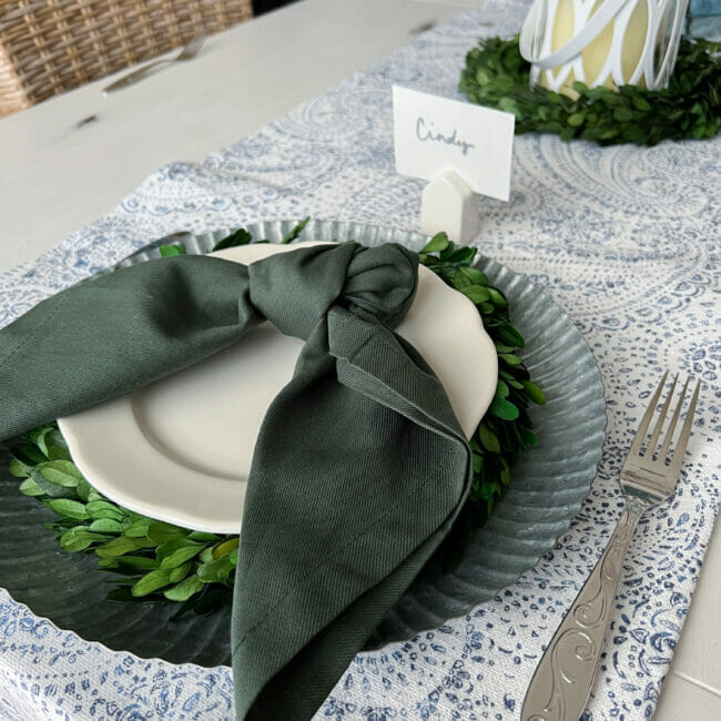 boxwood wreath under a white plate with a dark green napkin tied on top