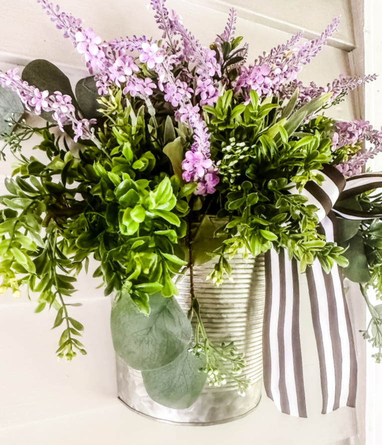 galvanized wall basket filled with boxwood, seeded eucalyptus and purple florals hanging on wall of gray house