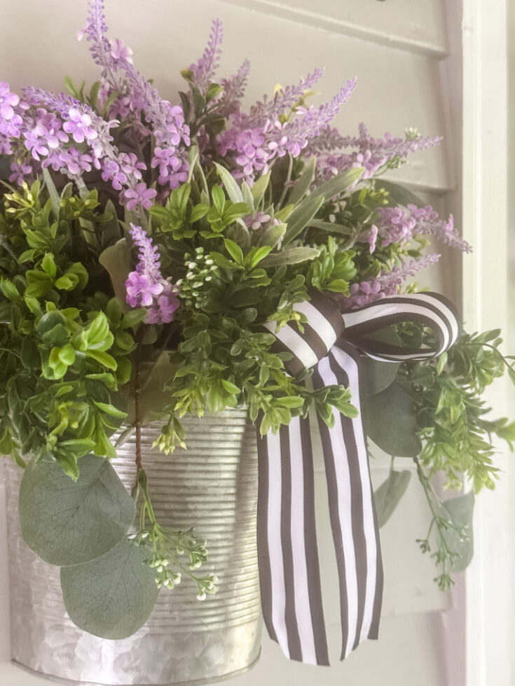 galvanized wall basket filled with boxwood, seeded eucalyptus and purple florals hanging on wall of gray house