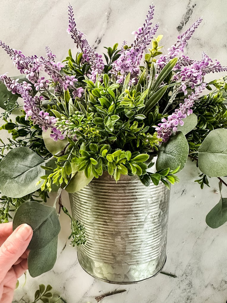 galvanized basket filled with artificial boxwood, purple flowers, and seeded eucalyptus