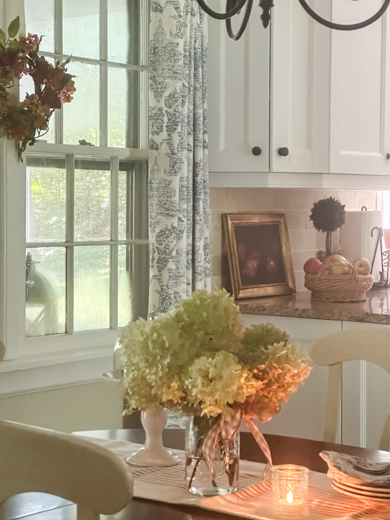 view of kitchen with white cabinets and kitchen table with dried hydrangeas candle and napkins