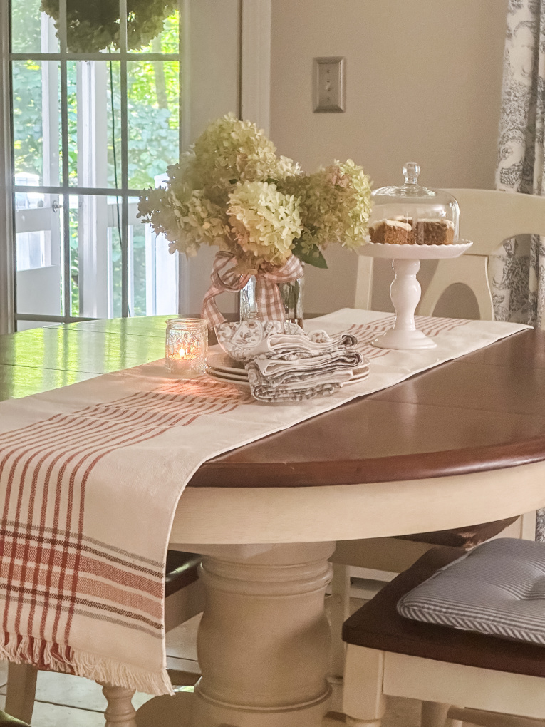 fall kitchen table with plaid runner, dried hydrangeas, napkins, plates, and pumpkin bars