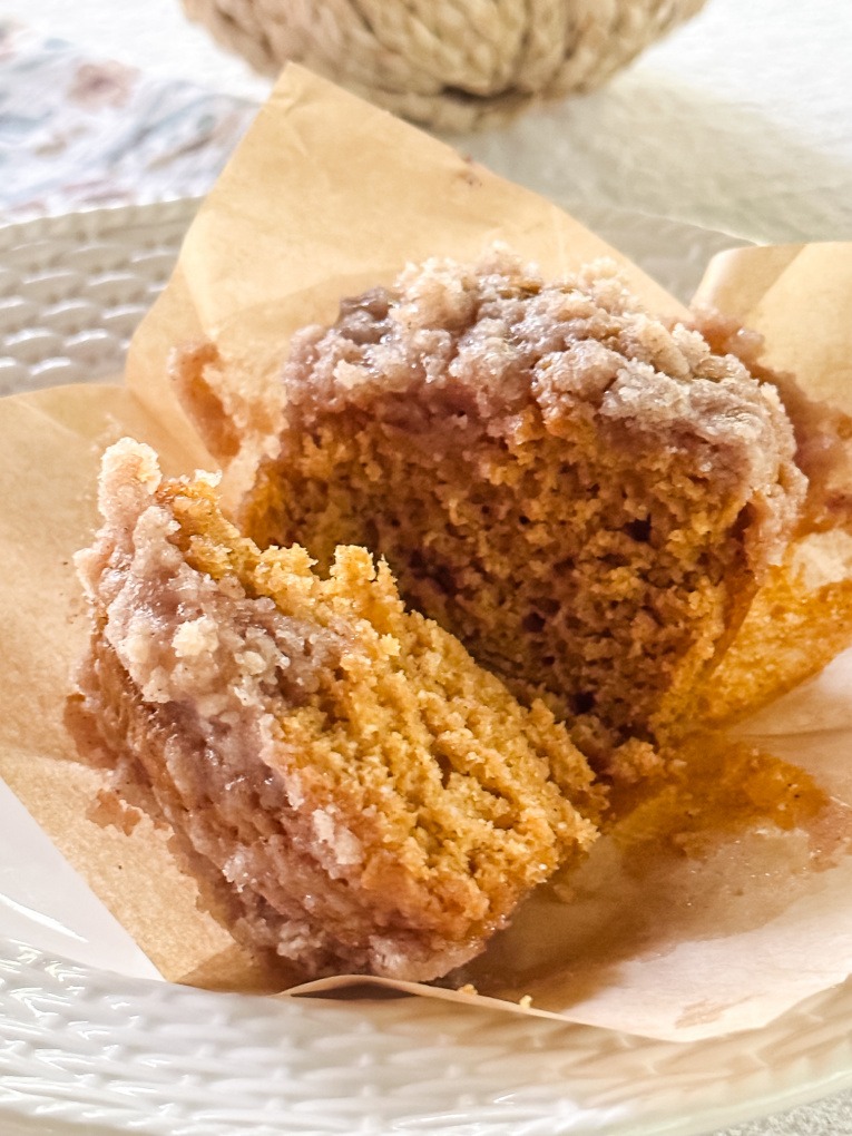baked pumpkin muffin with crumb topping cut in half, with muffin liner peeled away