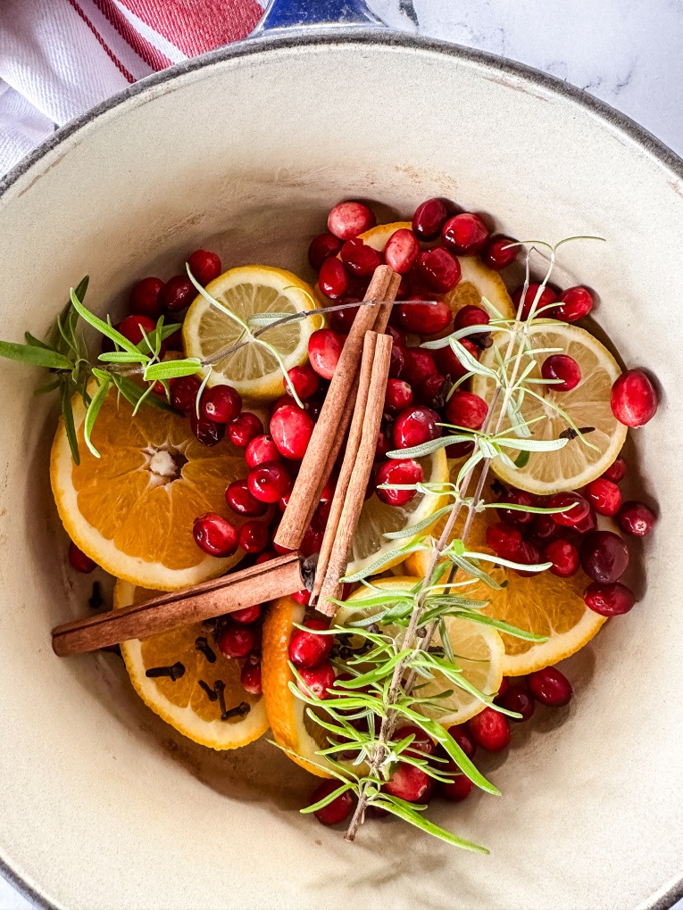 sliced oranges, lemon, cranberries, cloves, and rosemary in a pot with water