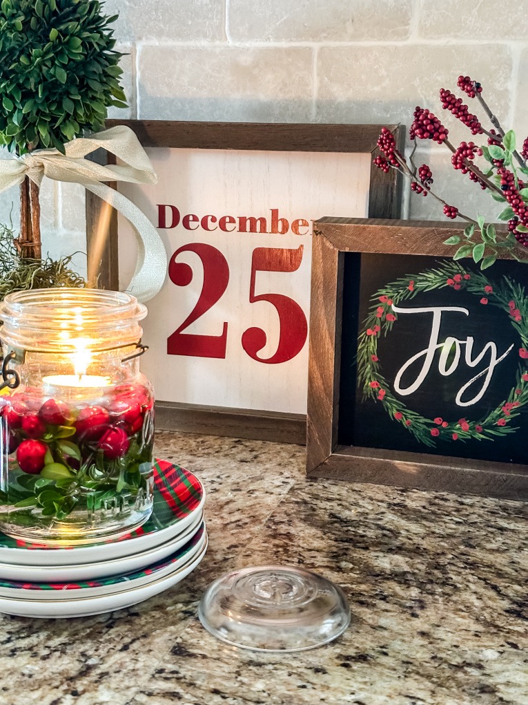 December 25 and Joy signs on granite counter with boxwood and cranberries in mason jar with candle