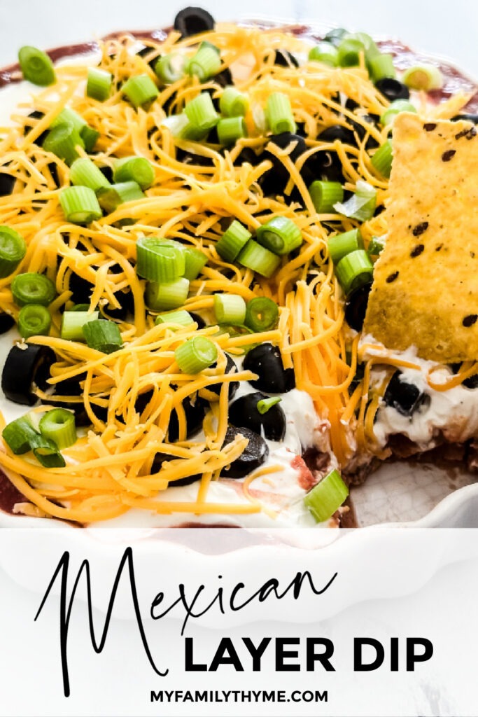 Mexican Layer Dip in a white round dish with a tortilla chip