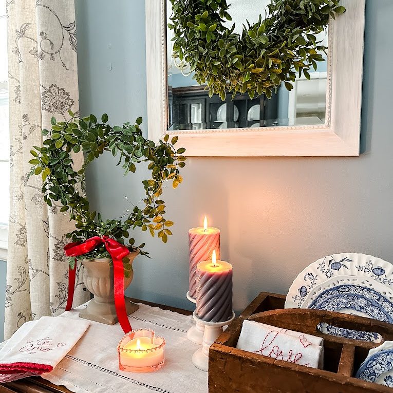 Heart-shaped topiary with lights and a red ribbon on side table with lit candles