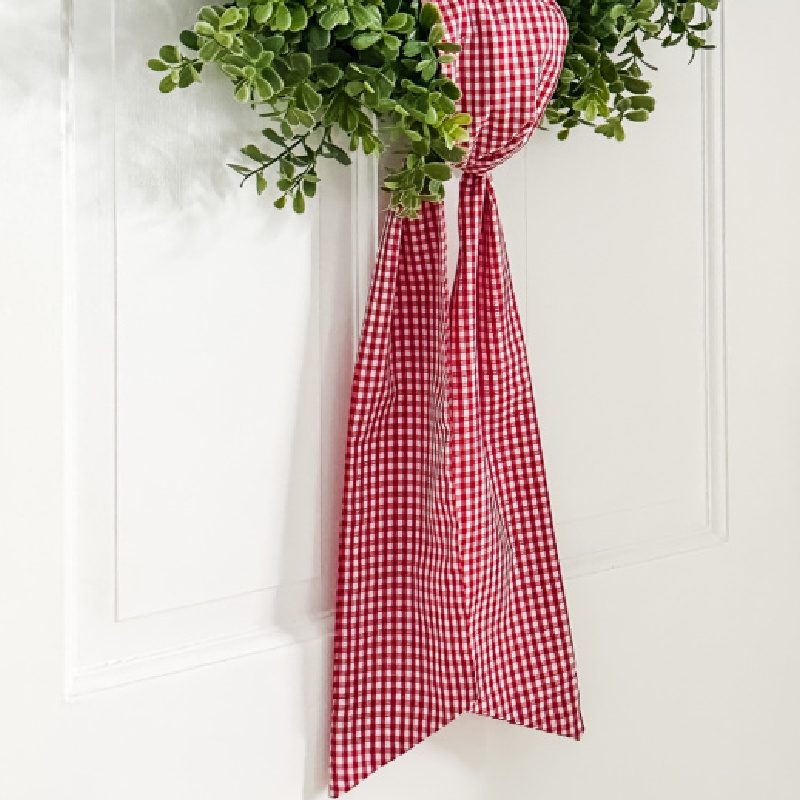 red and white gingham wreath sash on boxwood wreath hung on white interior door