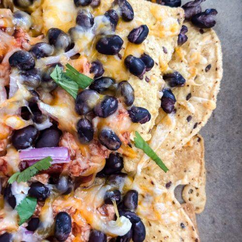 BBQ chicken sheet pan nachos on parchment lined tray with black beans, red onion, and melted cheese