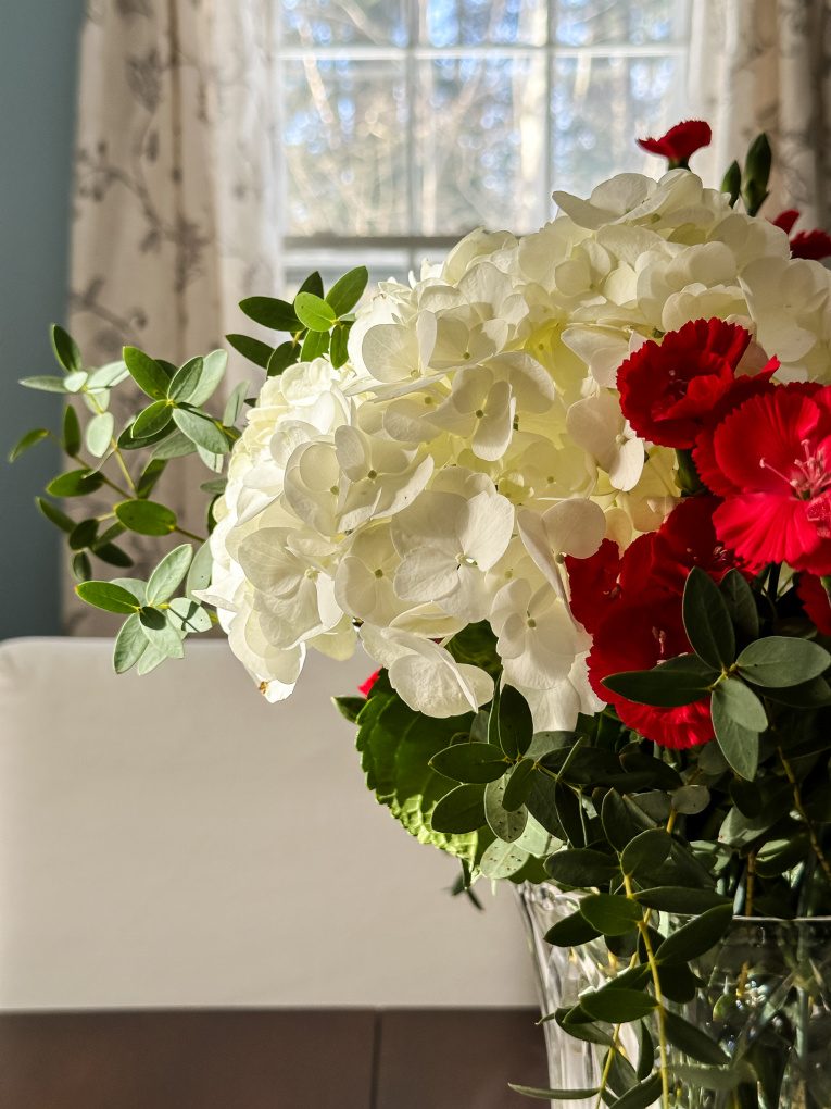 close up of white hydrangea with red carnations and greenery in vase