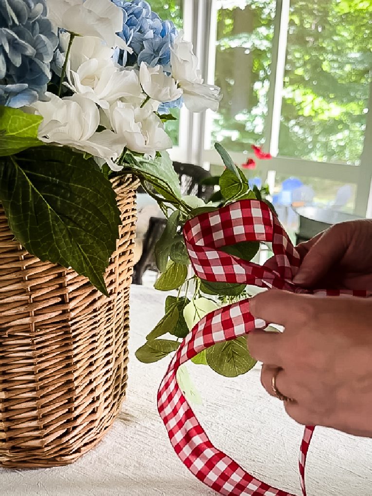 attaching red and white gingham bow with wire to flower filled wicker basket